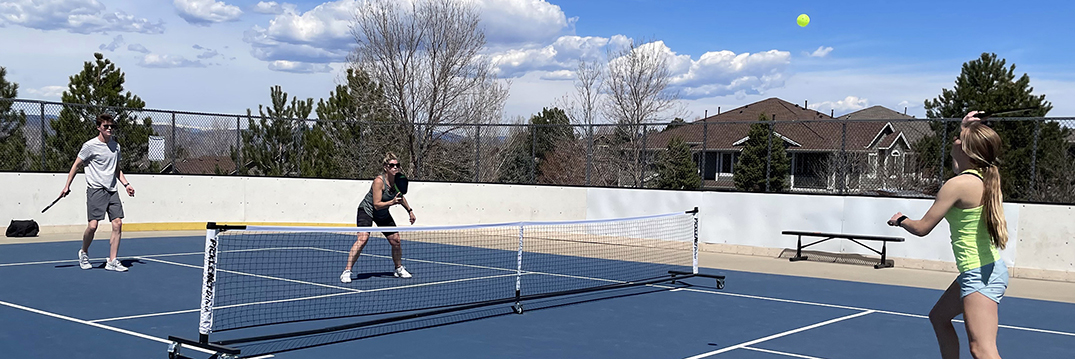 A multi-generational group plays pickleball on an outdoor court.