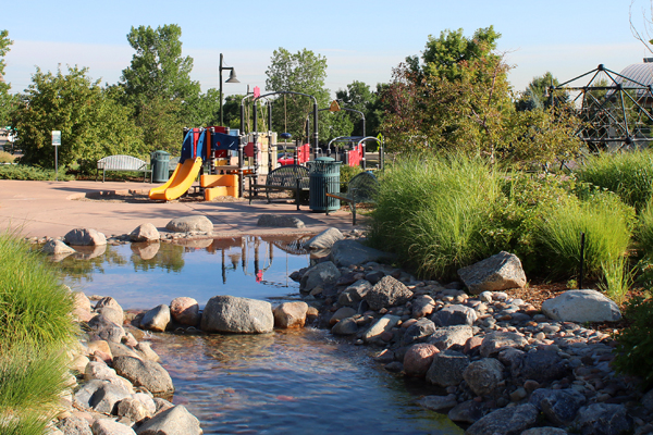 Civic Green Park's playground is framed by green landscaping and a wading stream.