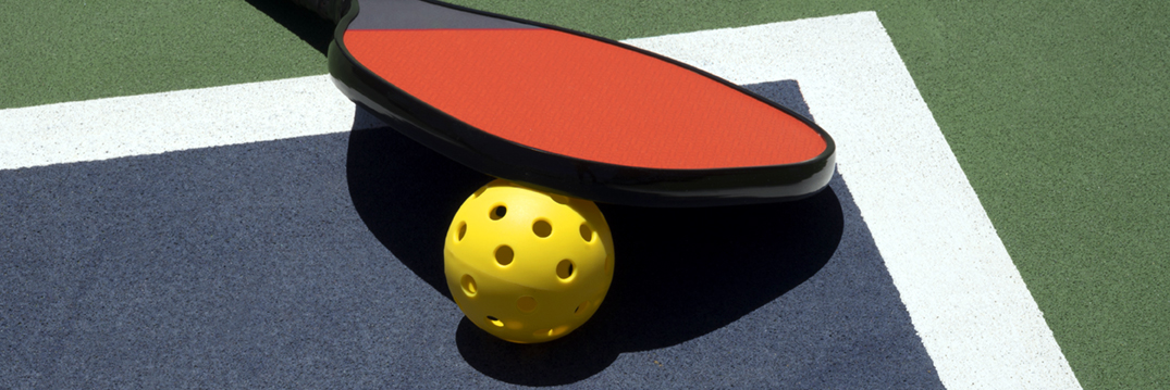 Close up of a pickleball paddle and ball.