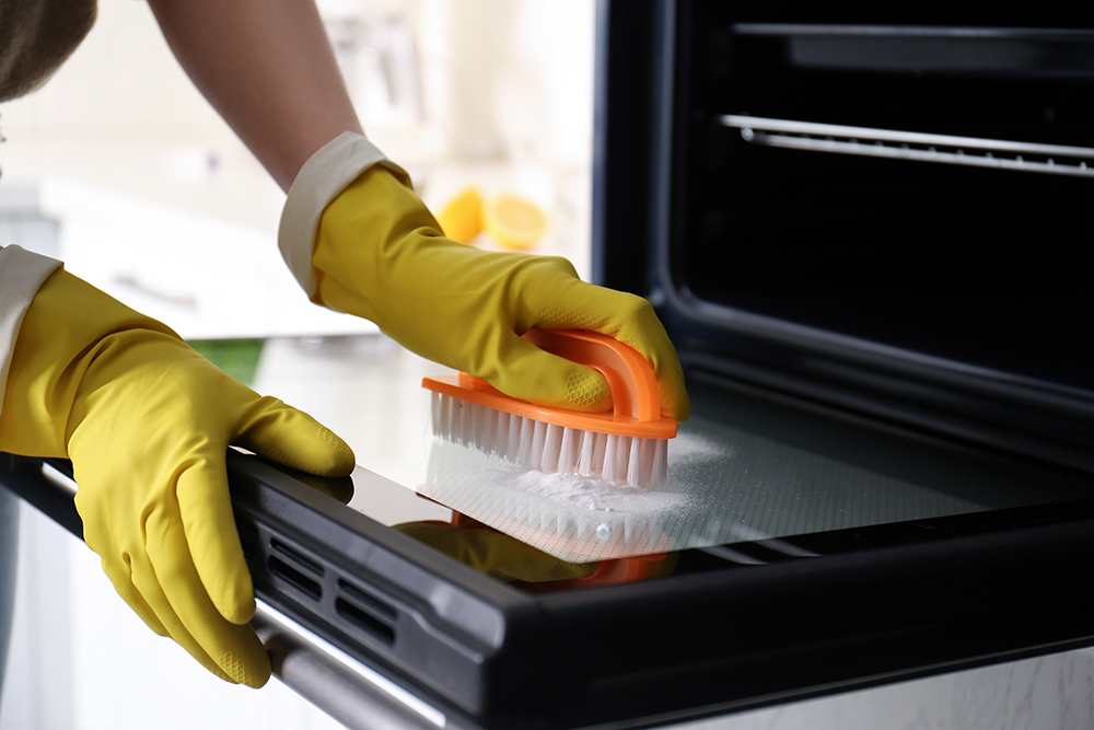 Person wearing gloves and cleaning their oven with baking soda paste.