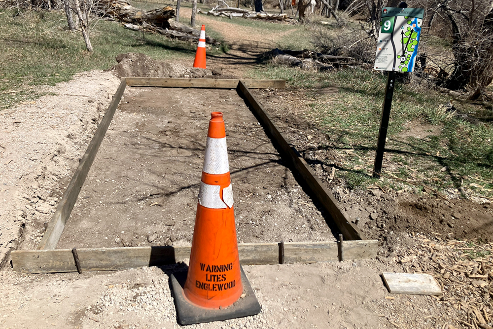 Orange safety cones surround a wood frame where a new concrete disc golf tee pad will be poured