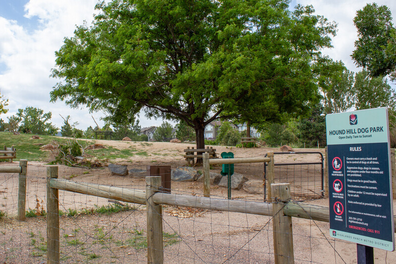 Hound Hill Dog Park's fenced in area with shady trees and a rules sign.