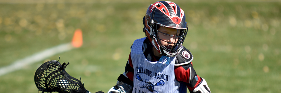 A young lacrosse player looks for an open teammate to pass to.