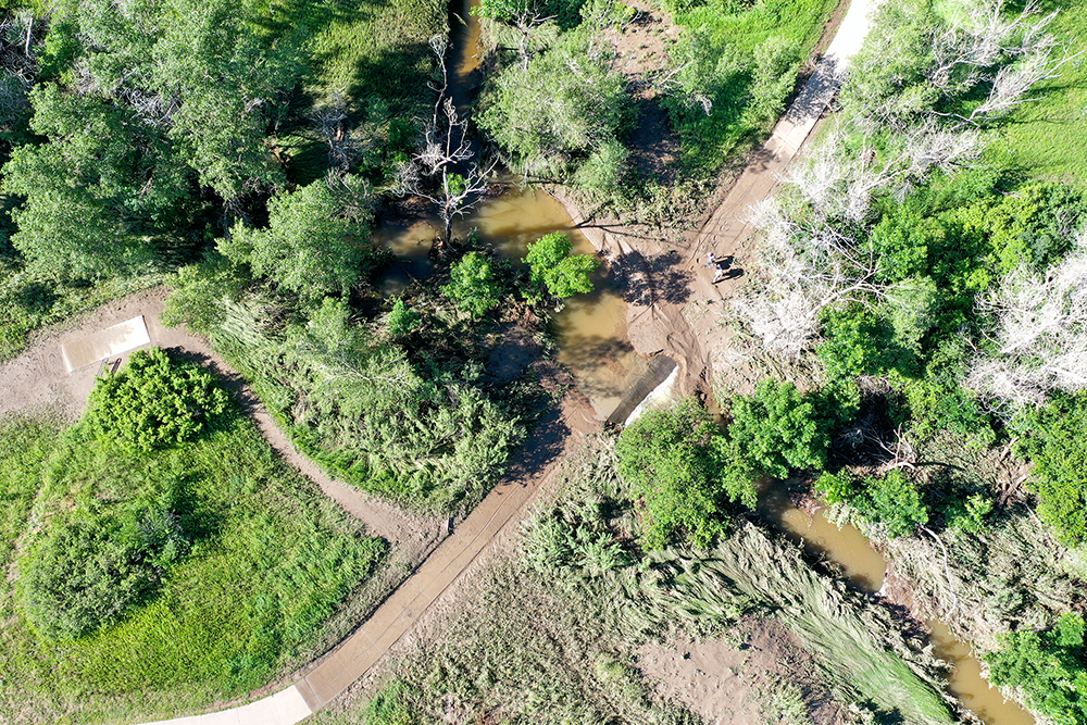 An aerial view showing sediment, debris, and flooding after a 2023 storm at the West Fork Disc Golf Course trail crossing.