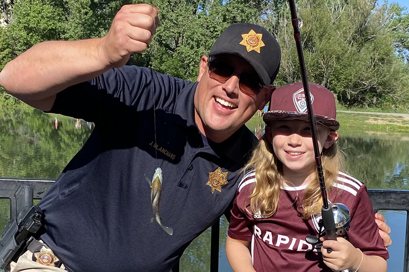 A sheriff's office deputy and a young angler smile and show off a fish caught during a pond fishing event.