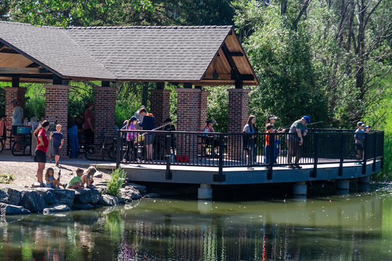 Visitors enjoy a large park shelter and fishing dock near a pond.