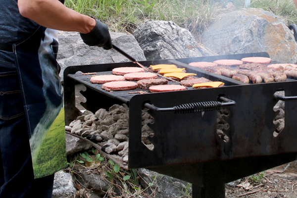 Hamburgers, cheeseburgers and brats are cooked over a charcoal grill in a park.