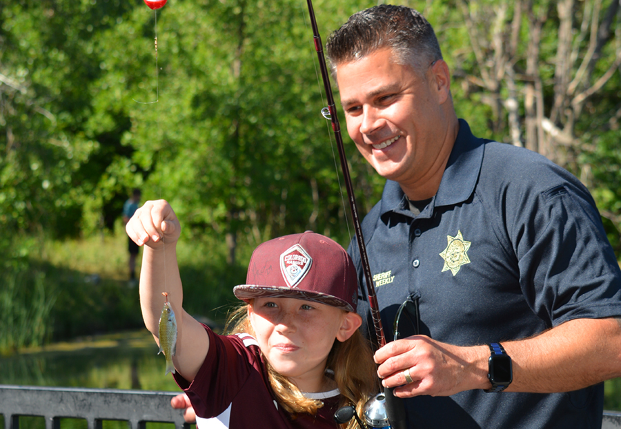 A kid and sheriff pose for a picture while holding up a fish caught from a pond.