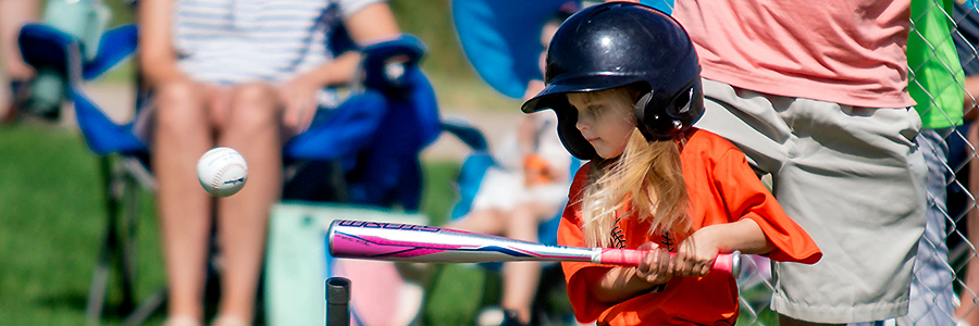 A young girl hits the ball off a tee during a game.